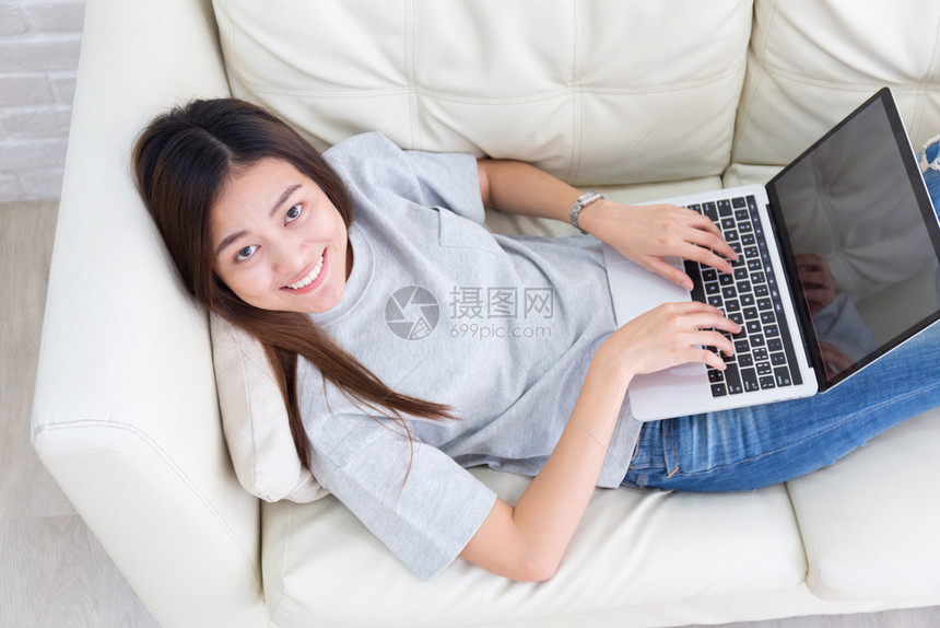 随意的技术在沙发上微笑并使用笔记本电脑的亚洲妇女最美景互联网图片