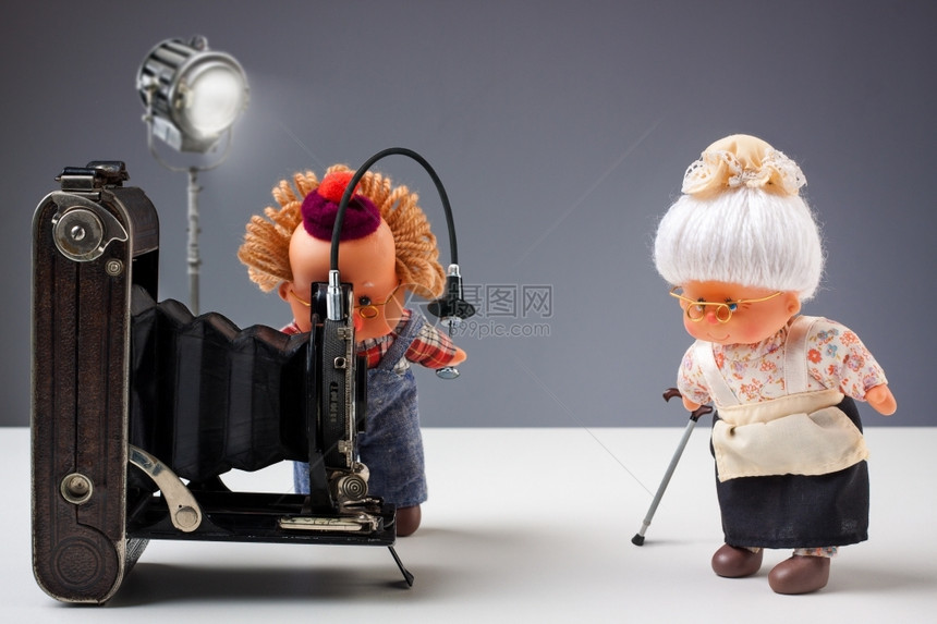 资深摄影师的木偶在演播室拍摄他老太的照片配有旧相机玩具娃优质的图片
