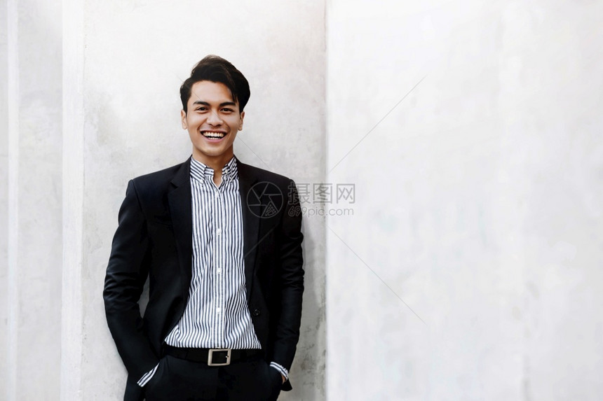 笑的亚洲青年商业家在城市中站着的无所事诉讼肖像望着一个快乐友善的人摄影机聪明亚洲人外部图片