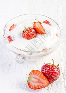 玻璃木制的红色白本底带草莓的新鲜有机酸奶图片