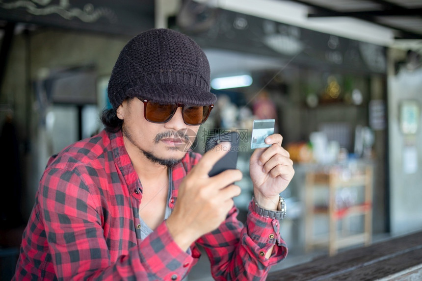 支付亚洲人应用程序潮人持有信用卡使手机在线购物现时的亚洲流行男子持有信用卡并使手机进行网上购物图片