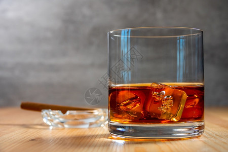 苏格兰小雪茄桌子上是一杯威士忌里面有冰块一烟灰缸张背景上还有雪茄在与冰一起的威士忌高球里图片
