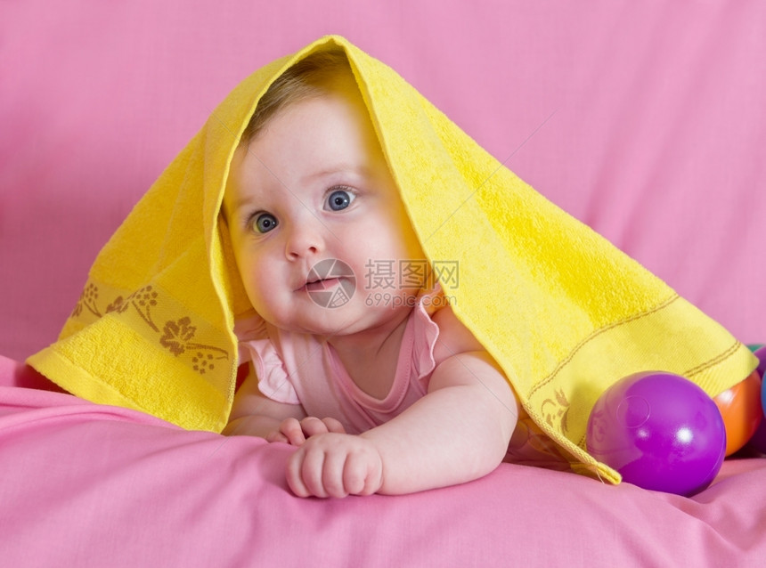 婴儿平静的甜美丽快乐女婴带着粉红背景的黄色毛巾图片