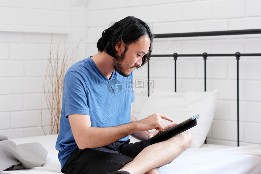 沟通学习信息年轻亚洲人坐在白室背景人和技术生活方式成人在线教育家工作时床上使用平板片的白人背景图片