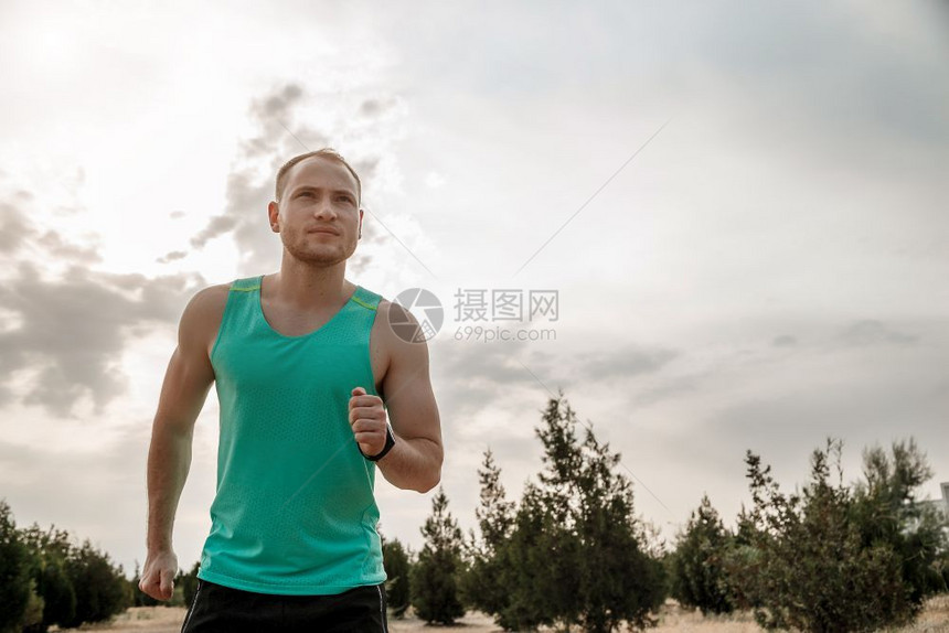 穿着蓝色T恤和黑短裤的白人男子日落时穿梭粗野地形训练年轻的运动男图片