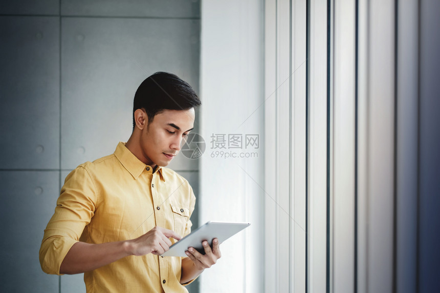 启动男人利用数字板块和微笑办公室的窗口站立在使用数字板和微笑的窗口旁自己图片