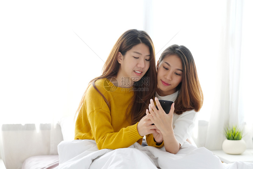 年轻可爱的亚洲女夫妇使用智能电话在家快乐地使用Igbt男女夫妇生活方式移动的快乐闺蜜图片