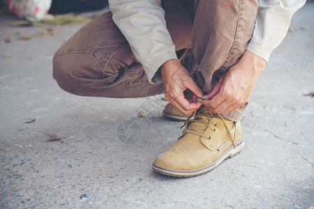 户外健康男人跪在地上为工人打领带鞋业靴子近距离拍到人手绑鞋的镜头为他建造筑用的棕色靴子紧贴男人把鞋子绑起来用做概念年轻的背景图片