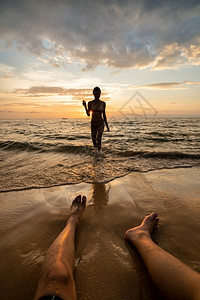 日落时沙滩上带男人腿的女子休光灯海滨金的脚图片