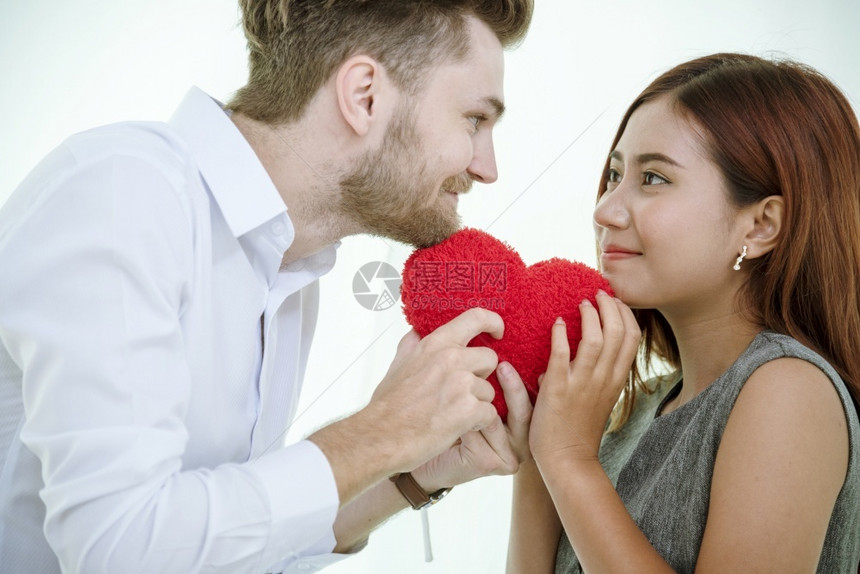 友谊情侣相爱的微笑和看着彼此与快乐的浪漫关系情伴侣持有红色心脏形状的爱红心象征近距离亲一见情友年轻的人们图片