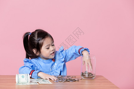 财政数商业这小女孩在一杯玻璃罐里捡到硬币钱储蓄的概念图片