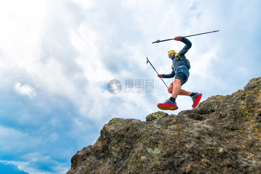 棍子鞋男运动员在山径上进行实践训练时带着棍棒跳过悬崖而摔倒在上图片