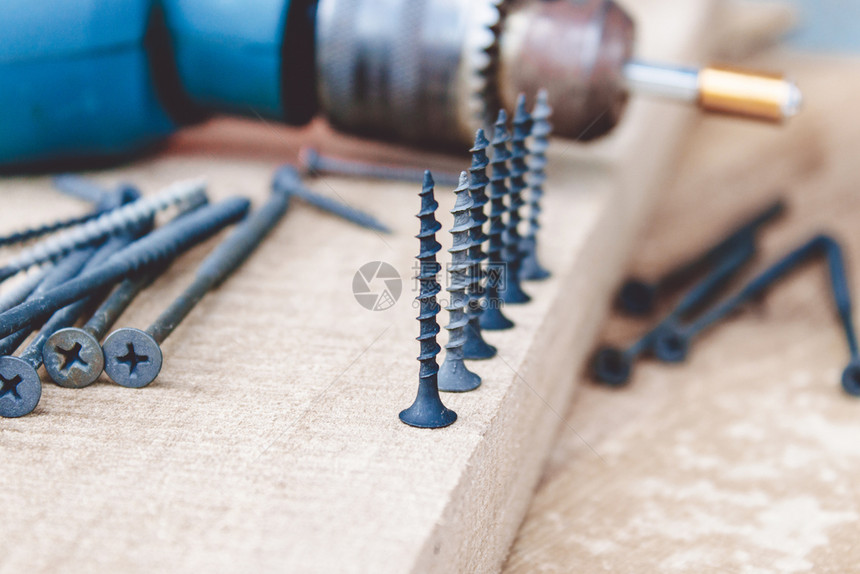 电的黑螺丝在木板背景的电钻附近排成一工具和维修作的概念钢螺丝金属黑在木板背景上的电钻附近排成一工具和维修的概念理工作钢螺丝业的铁图片