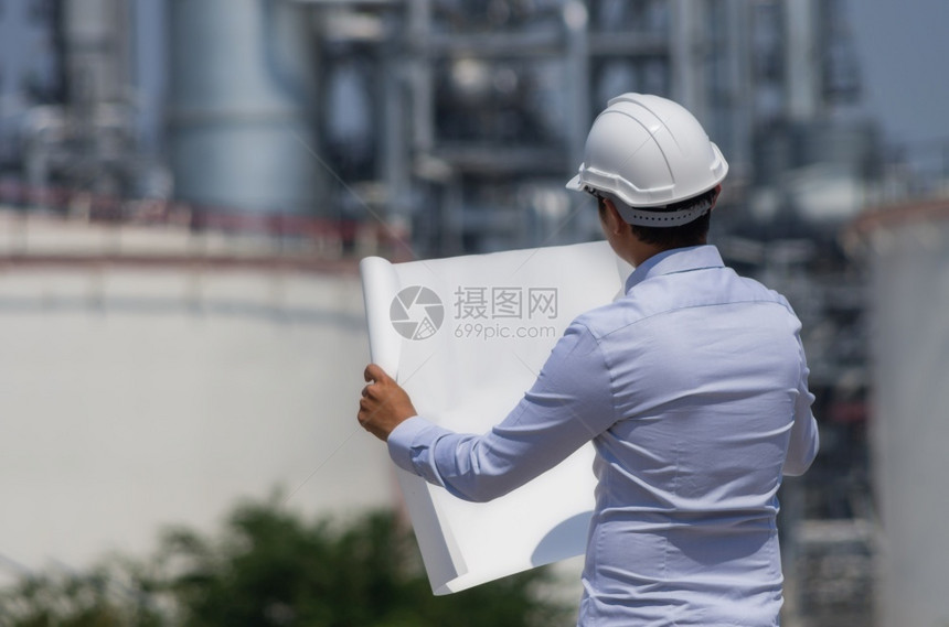 力量工程师身着白头盔站在炼油厂背景上站立的炼油厂工程师作气体图片