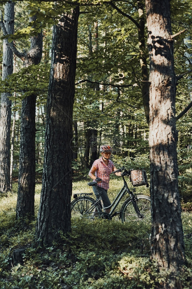 活跃的女在森林里骑自行车度过免费的暑假戴着自行车头盔和手套的女拿着自行车和篮子站在树后活跃的女在森林里骑自行车度过免费的暑假女士图片