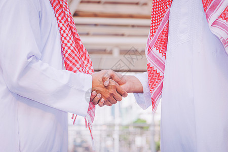微笑阿拉伯商人在建筑工地上与商业伙伴握手并与之种族团队合作图片