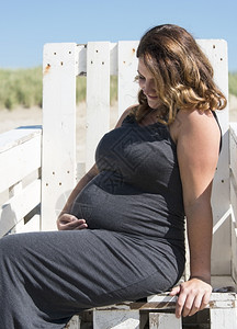 坐在沙滩上木椅的成年快乐怀孕妇女父母期待生育图片