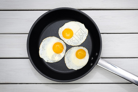最佳白色的烹饪3个阳光明媚的侧面顶端景色在木制白桌上的黑锅里煎鸡蛋图片