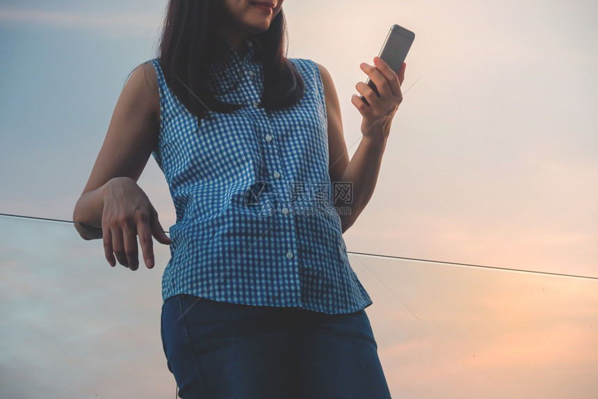 联系经过电子的现代人生活方式概念通过阅读数据或信息让青年女轻松起来夏季在河滨的顶峰Deck使用智能手机站台图片