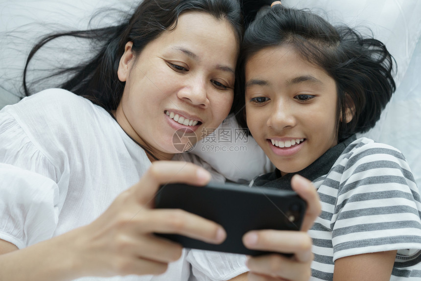 手机父母互联网在床上玩电话游戏的亚洲母亲和女儿妇孩在卧室里如此快乐与欢她们一起在床上玩着电话游戏图片
