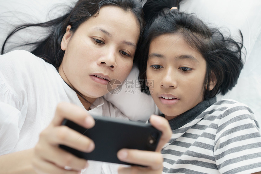 亚洲人互联网在床上玩电话游戏的亚洲母亲和女儿妇孩在卧室里如此快乐与欢她们一起在床上玩着电话游戏美丽的图片