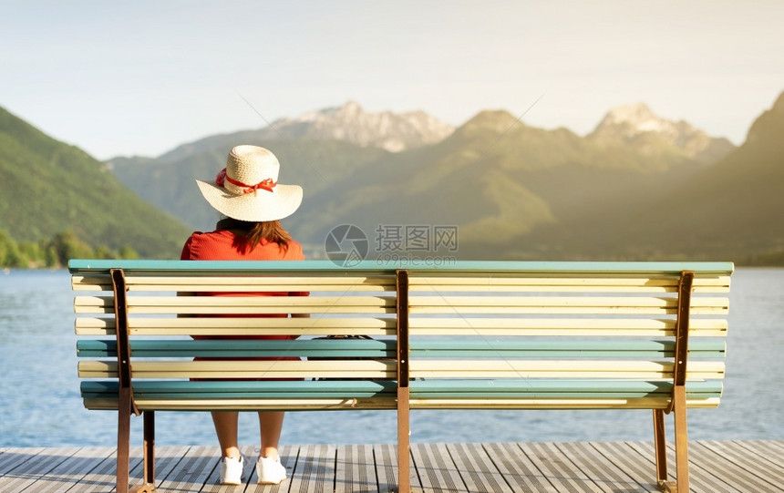 女孩坐在长椅上戴着跟踪帽子穿红色礼服仰望着山地看湖边的生活方式概念阿讷西夏天放松图片