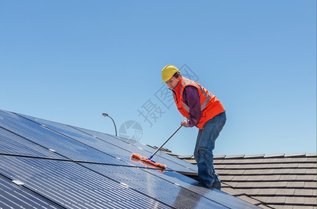 在房顶打扫太阳能电池板的青年工人图片