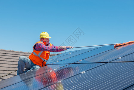 在房顶上打扫太阳能电池板的青年工人图片