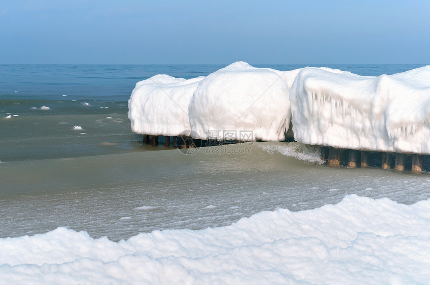 海浪在冰冷的雪泥中在海的防波堤上结冰在冬天的海岸中防波堤上冰在冷雪泥中海浪在冬天岸白色景力量图片
