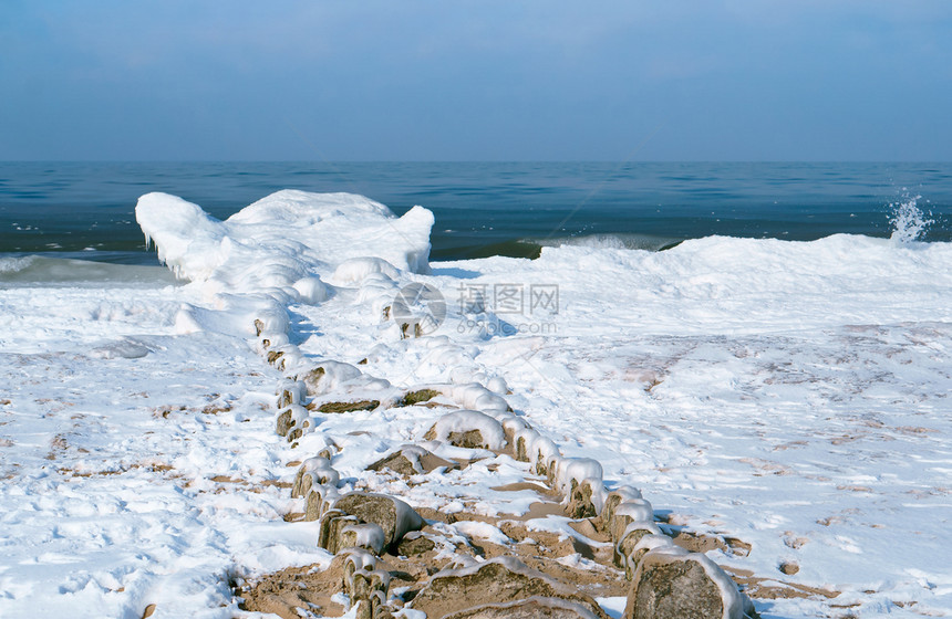 海浪在冰冷的雪泥中在海的防波堤上结冰在冬天的海岸中防波堤上冰在冷雪泥中海浪在冬天岸木制波浪天空图片