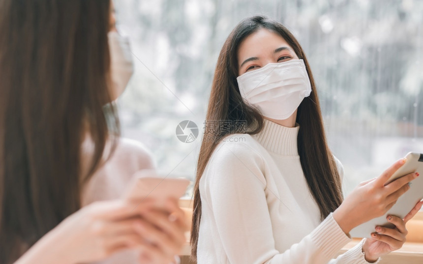 亚洲人在咖啡店使用平板药时戴面罩保护的亚裔妇女新常态和社交偏移概念女上市图片