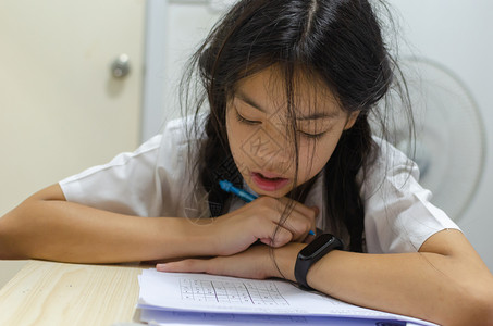 身着校服的美丽亚洲年轻女孩想在餐桌上做家庭作业瞳孔学生脸图片