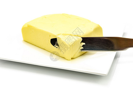 银器新鲜的用刀在盘子上的黄油片以白色背景隔绝特写图片