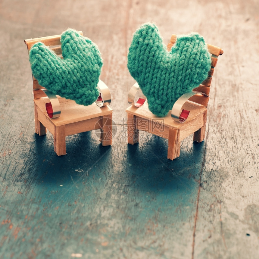 座位坐两颗心要在一起情侣像插图一样相爱照顾和护绿色心放在手工制作的迷你家具上作为椅子摇摆在木本底床上针织的图片
