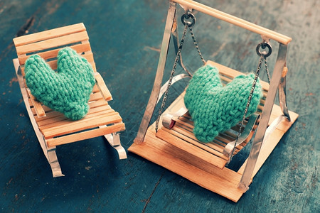 针织的两颗心要在一起情侣像插图一样相爱照顾和护绿色心放在手工制作的迷你家具上作为椅子摇摆在木本底床上关心漂亮的背景图片