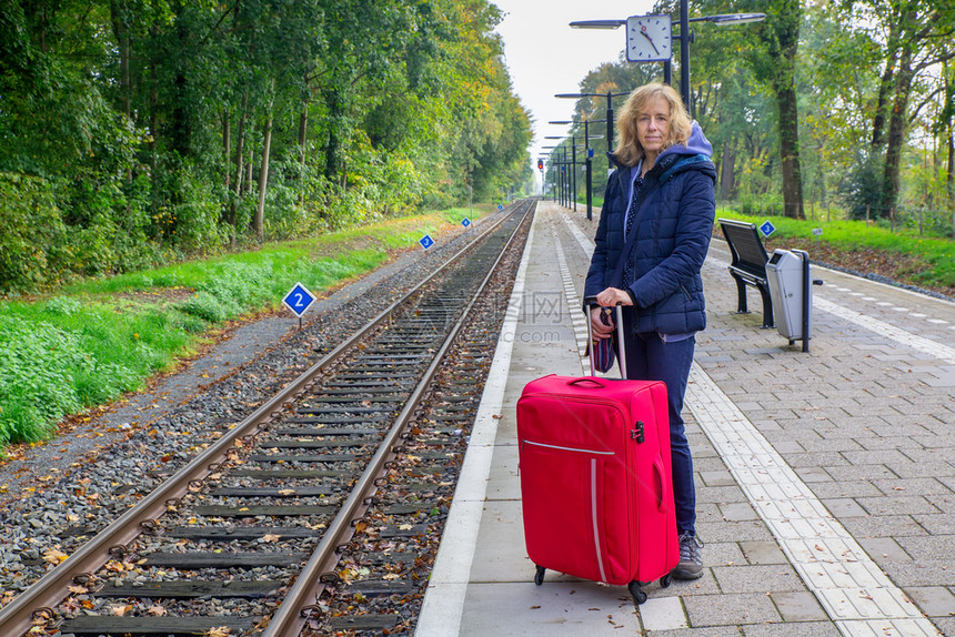 站在火车着的有红色手提箱白种妇女常设假期德尔登图片