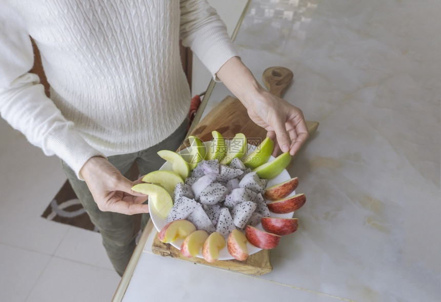 盘子身穿白长袖的部分妇女正在家厨房的大理石柜子上准备红绿苹果和龙并准备红绿苹和龙内部的健康图片