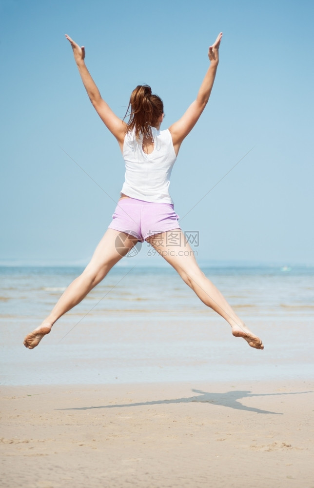 蓝色的玩青年美丽精力充沛年轻女子在海滩上跳跃图片