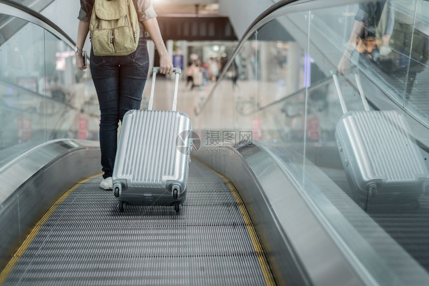 大约旅行搭乘飞机前往世界各地的女游客在机场终点站自动扶梯上乘坐的女旅游者携带行李手提箱到世界各地去降低图片