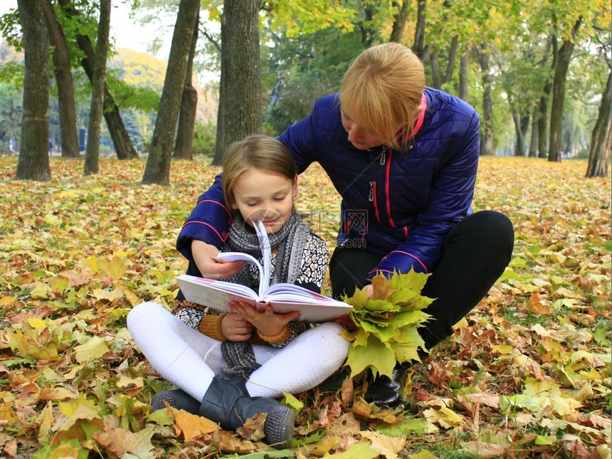 婴儿黄色的休息母亲和女儿在秋天公园读一本书母亲和女儿在秋季城市公园读一本书图片