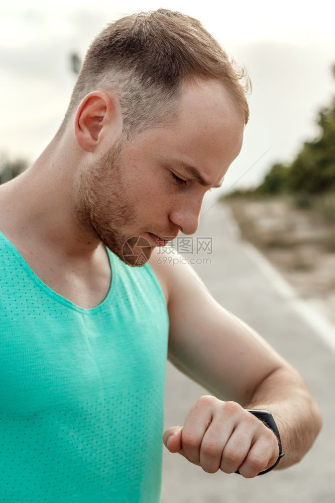 强的积极在慢跑之后或前看健身追踪器读数的白种人T恤肖像画检查图片