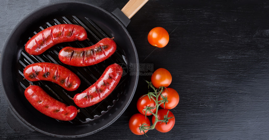 美味的抽烟黑煎锅上炸烤香肠和西红柿从上方复制空间的黑背景视图在煎锅上加西红柿的油味香肠辛辣图片