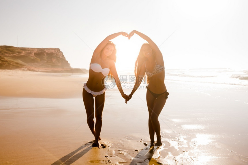 手美丽女孩们在沙滩上用双臂创造心图片