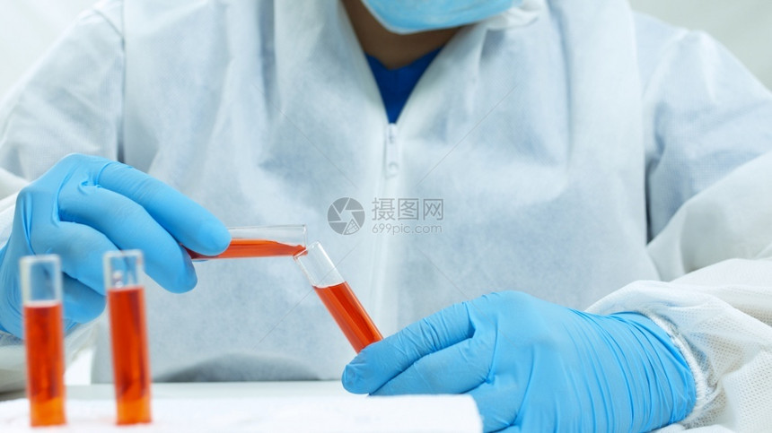 研究员身穿生物防护服面罩和蓝色手套的拉丁医生在白色背景的两个玻璃试管之间混合红色液体的特写视图身穿生物防护服面罩和蓝色手套的拉丁图片