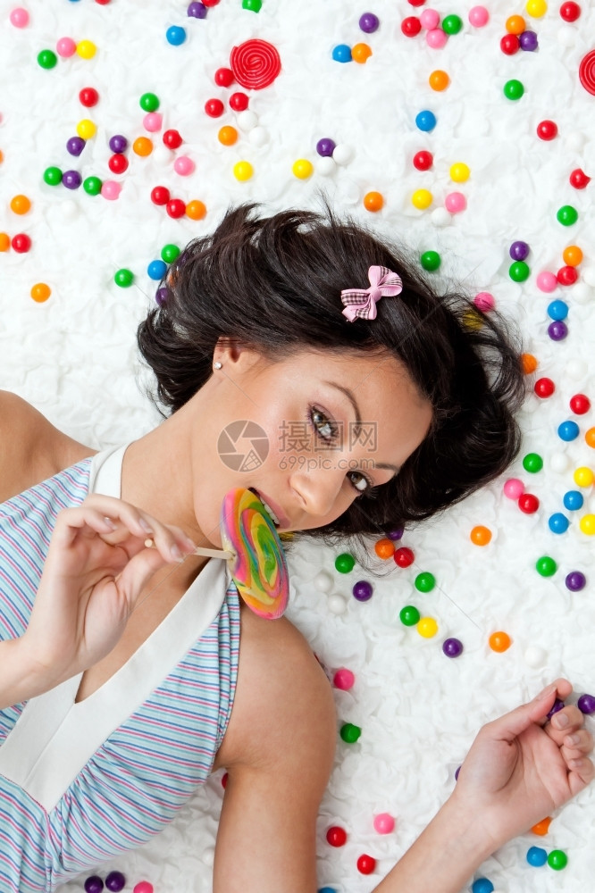 年轻的拉丁女人躺在乌云上像地板一样在吃棒糖的多彩泡金球之间拉丁裔蓝色的摄影图片