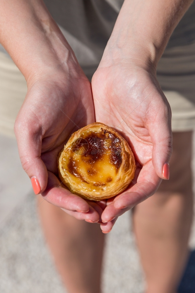 在葡萄牙里斯本的背景点上葡萄牙传统妇女手中的Pasteisdenataspathesnata小吃食物甜点图片