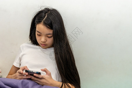美丽玩身穿白色T恤衫的年轻女孩随便看家里的智能手机Copy空间可爱的图片