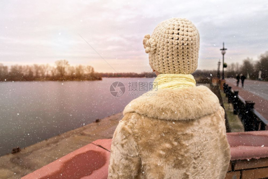 中间薄片外部一位穿着羊毛帽和皮外套的女人在雪下寒冷而悲伤的冬天清晨看着河图片