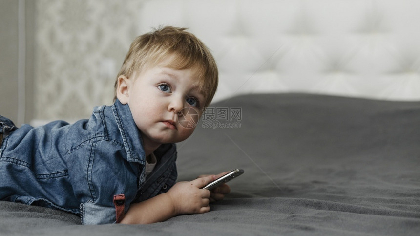 小工具年轻的拿着手机男孩在床上睡觉技术图片