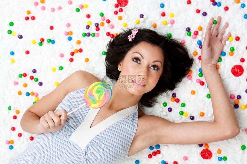 糖果年轻的拉丁女人躺在云层上像地板一样在多彩的泡糖球之间拿着棒糖女士图片